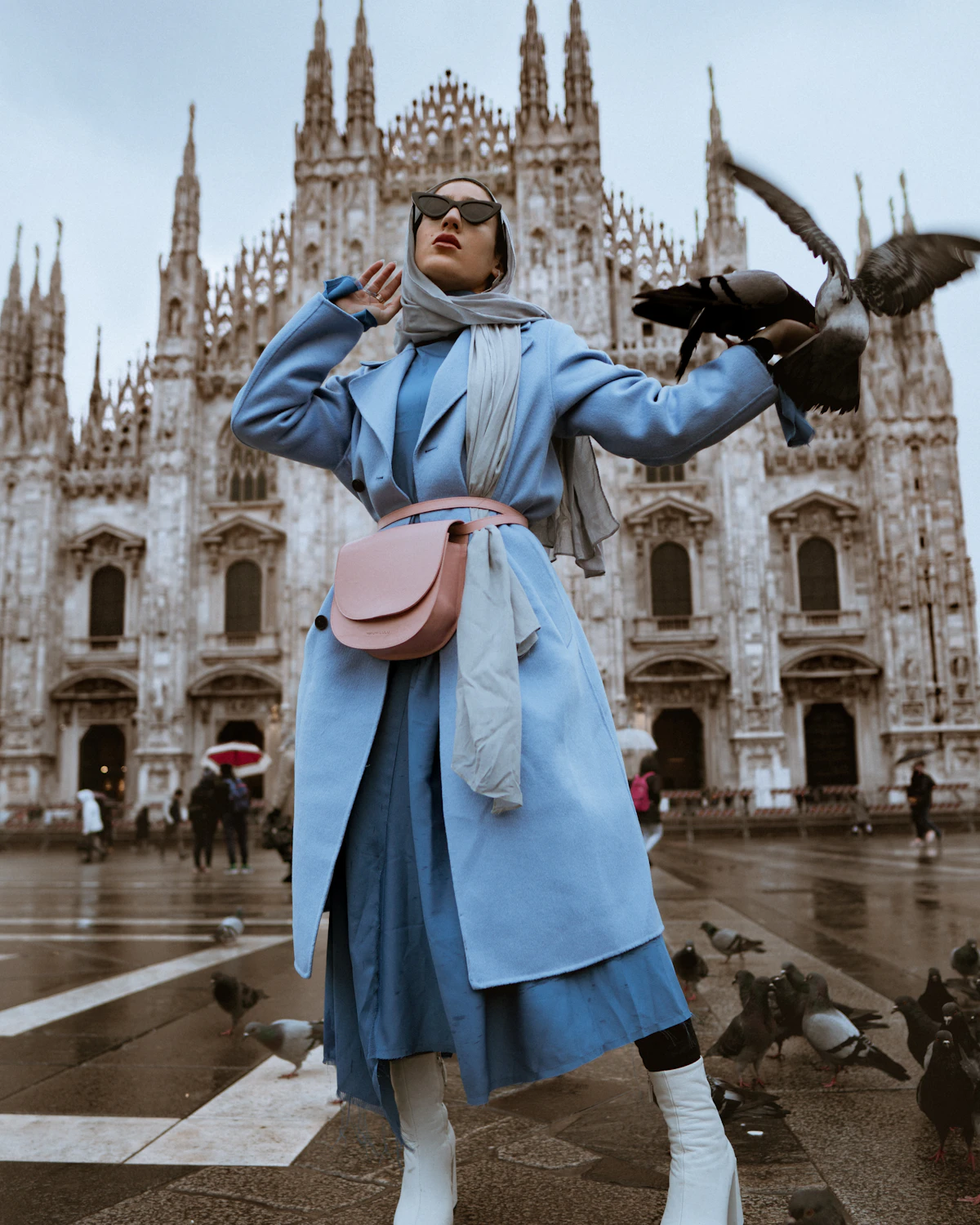 A person in a pale blue coat and scarf in a European city square.