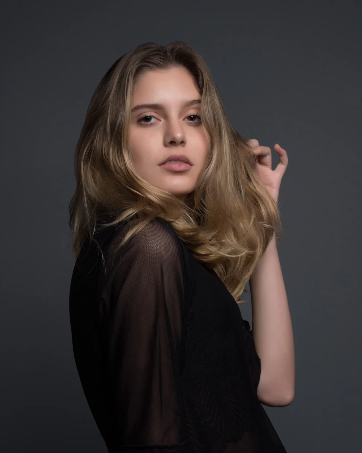 Editorial studio portrait of a model in a black sheer blouse.